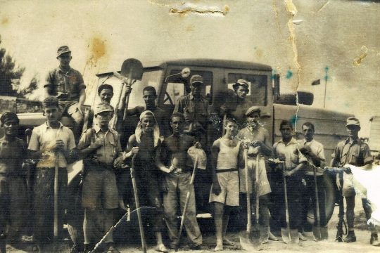 Συνεργείο καταναγκαστικής εργασίας σε ολιγόλεπτη διακοπή. Ενοπλοι φρουροί επιτηρούν τους ξυπόλητους νεαρούς ομήρους. Δεύτερος εξ αριστερών ο Ευάγγελος Θεοδωρόπουλος (1926-1999) από τις Μηλιές Πηλίου